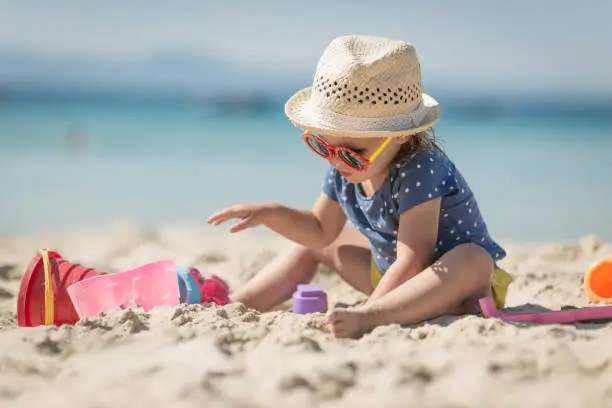 Photo of Caucasian littplayng beach toysle girl with hat