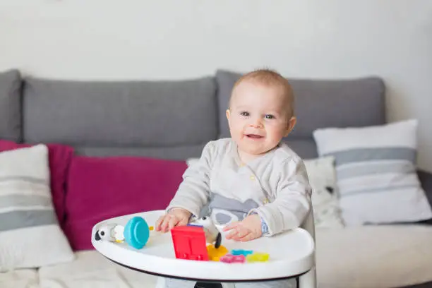 Photo of Cute baby boy, playing with toys at home, sitting in high chair