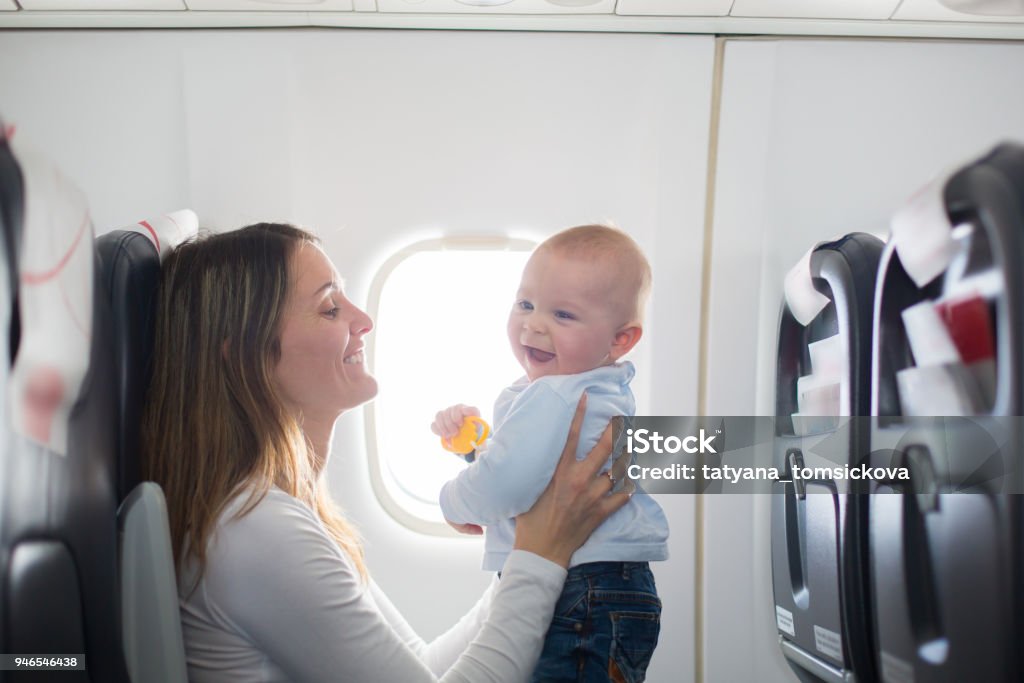 Young mom, playing and breastfeeding her toddler boy on board of aircraft Young mom, playing and breastfeeding her toddler boy on board of aircraft, going on holiday Baby - Human Age Stock Photo