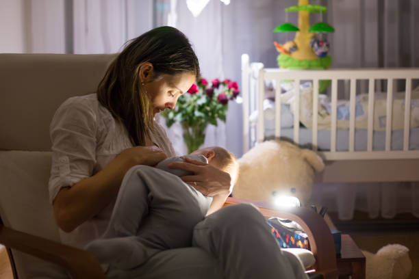 Young beautiful mother, breastfeeding her newborn baby boy at night, dim light Young beautiful mother, breastfeeding her newborn baby boy at night, dim light. Mom breastfeeding infant low lighting stock pictures, royalty-free photos & images