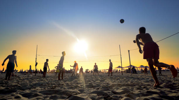 beach volleyball silhouette during sport recreation at summer vacationat sunset - volleying sport summer men imagens e fotografias de stock