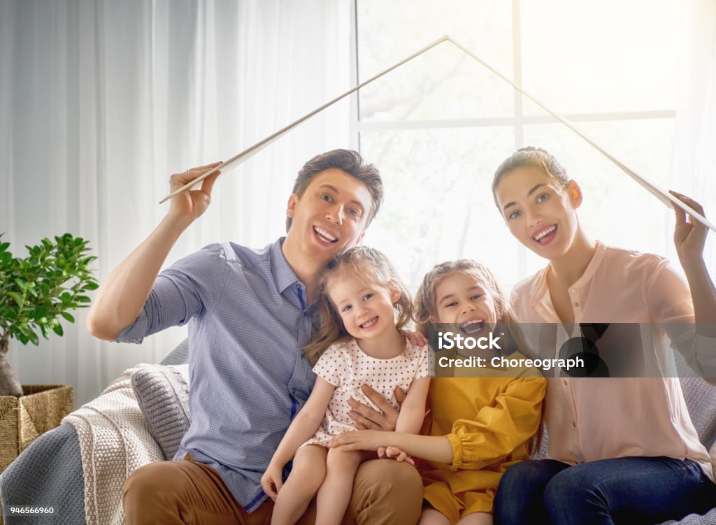 Concept of housing for young family Mother, father and children girls in the room with a symbol of roof. Concept of housing for young family. Insurance Stock Photo