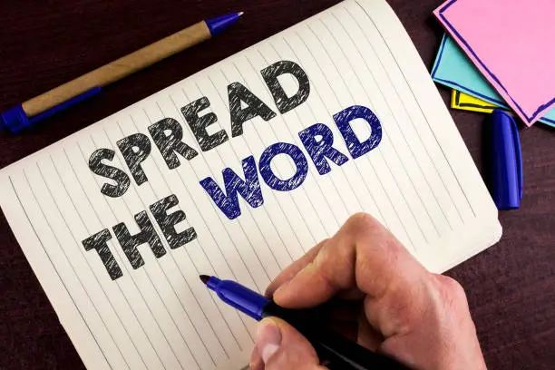 Photo of Conceptual hand writing showing Spread The Word. Business photo showcasing Run advertisements to increase store sales many fold written by Man on Notebook Book on wooden background Pen.