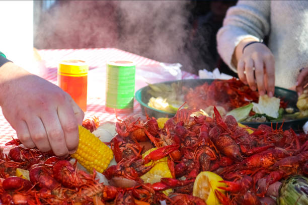 alcanzar en un pedazo de maíz en la mazorca de una pila de comida al vapor en camarones ebullición con la otra mano recogiendo comida de una bandeja en el fondo - enfoque selectivo de la mano - steam steamed lemon food fotografías e imágenes de stock