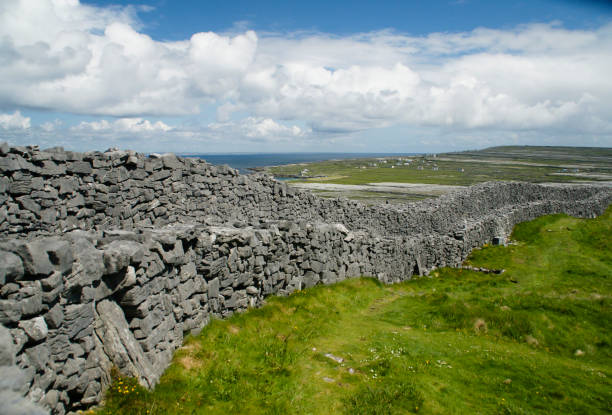 Outer Wall of Dun Aonghasa (Dun Aengus) with Island Landscape The view east, northeast from an outer enclosure of Dun Aonghasa (Dun Aengus) looking along the outer concentric wall, the exceptional dry stone and walkway visible.  Here the land falls away to review a view of Inishmore karst landscape, the coast and Galway Bay. michael stephen wills aran stock pictures, royalty-free photos & images