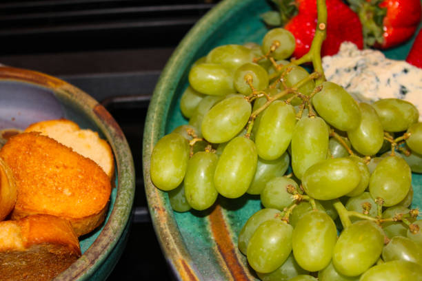 uvas verdes, servidos en bandeja de barro con fresas y pan closeup - heath ceramics fotografías e imágenes de stock