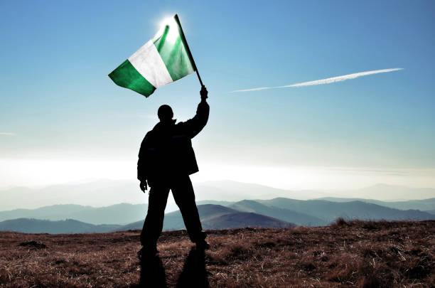Successful silhouette man winner waving Nigeria flag on top of the mountain peak stock photo