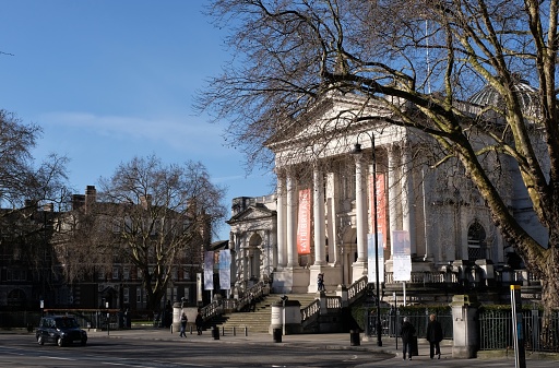 London, England - February 16, 2018: the main entrance to Tate Britain in Millbank (near Westminster) next to the River Thames, London. Tate Britain houses the UK’s national collection of British art and hosts several major art exhibitions each year.  In the photo, a London black cab waits at the foot of the main staircase to the gallery.