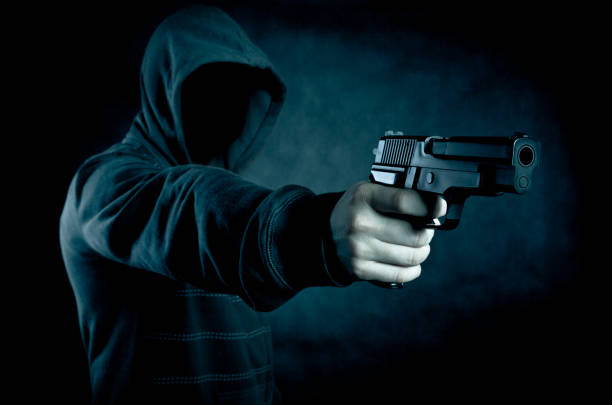 istock Hooded man with a gun in the dark 946610320