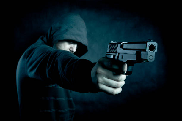 istock Hooded man with a gun in the dark 946610326