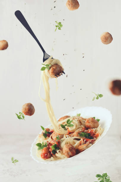 летающая еда. левитация пасты феттуччине с фрикадельками, томатным соусом, базиликом на белом фоне - spaghetti sauces pasta vegetable стоковые фото и изображения