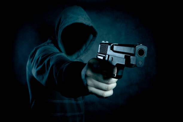 istock Hooded man with a gun in the dark 946610404