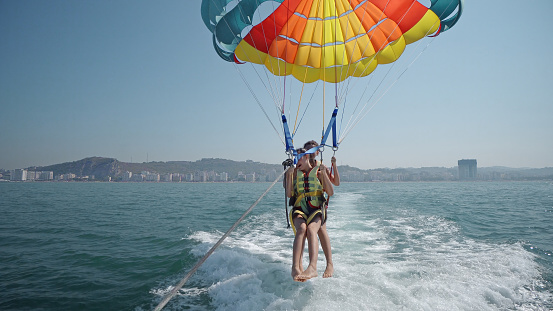 Parasailing water amusement. Flying on a parachute behind a boat on a summer holiday by the sea in the resort. Beautiful bright blue water and colorful parachute