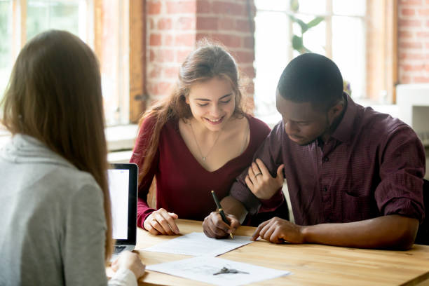 multiracial couple signing deal from real estate agent - women men signing business imagens e fotografias de stock