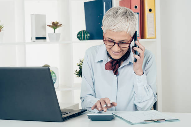 istock Mature woman calculating and using phone at office 946654720