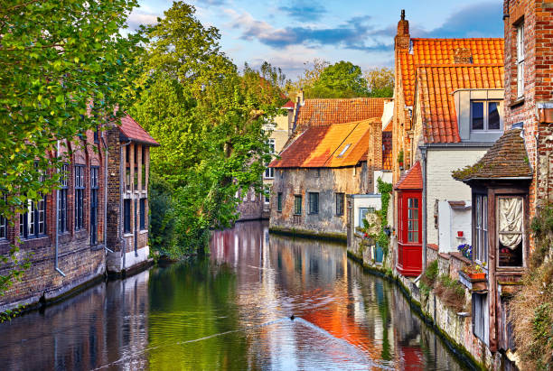 Bruges Belgium medieval ancient houses Bruges, Belgium. Medieval ancient houses made of old bricks at water channel with boats in old town. Summer sunset with sunshine and green trees. Picturesque landscape. flanders belgium photos stock pictures, royalty-free photos & images