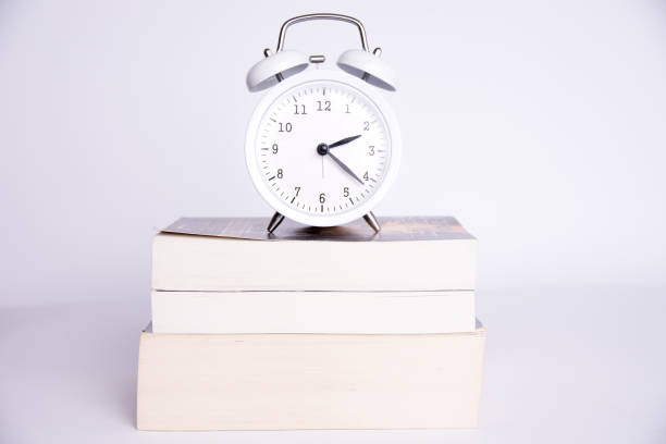 istock clock standing on the books on a white background 946676176