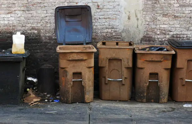 Trash, cooking oil, garbage cans in an alley.