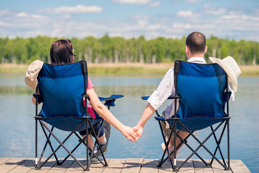couple sitting on chairs at the pier near the lake and holding hands