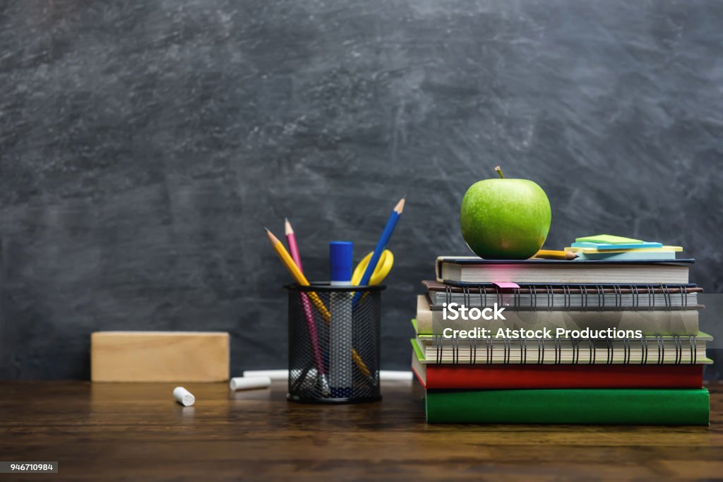 Books, stationery and education supplies on wooden desk in classroom Books, stationery and education supplies on wooden desk in classroom with blackboard in background Teacher Stock Photo