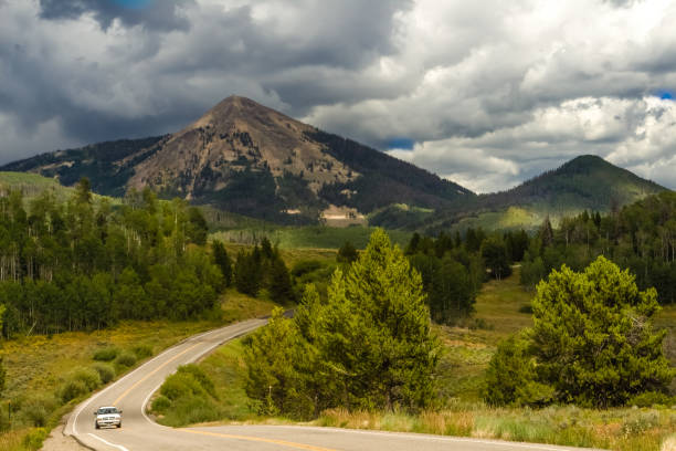 Mountain road before a storm View of a road between mountain peaks in Colorado, USA; stormy clouds about the peaks; one car driving steamboat springs photos stock pictures, royalty-free photos & images