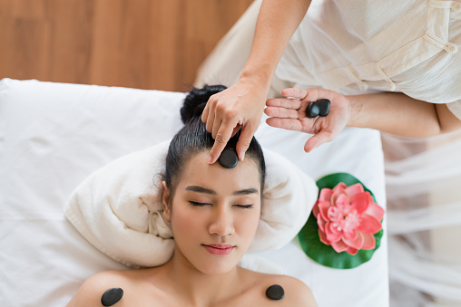 Young beautiful Asian woman relaxing having facial massage with mineral stone in the spa