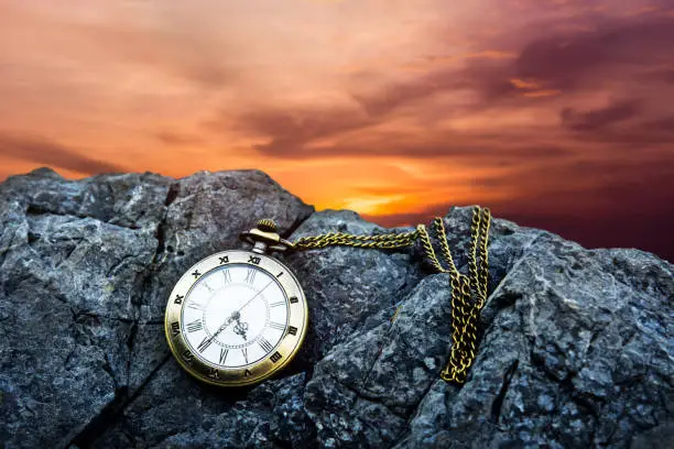 Time Concept. Vintage Golden Pocket Watch on island rock, Sunrise or Sunset Sky as background