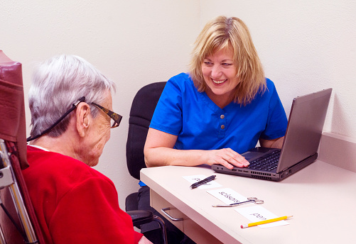Blond Caucasian speech language pathologist laughs with a senior aged female aphasic patient during speech therapy session targeting visual  comprehension skills. Patient realized she incorrectly matched objects to a field of three single written words.