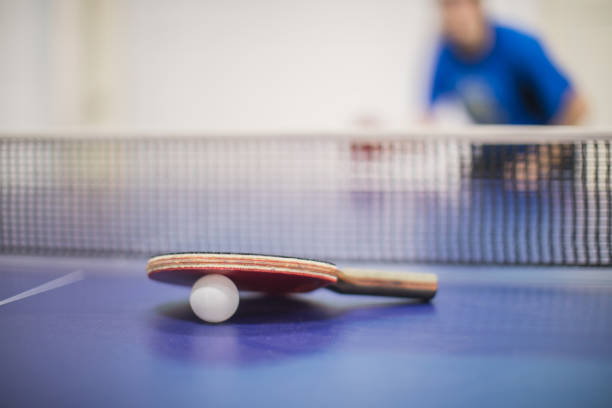 Young ping pong player playing table tennis game. He is holding a red racket. He is very concentrated. Behind him, the stadium with the fans in the defocus.
