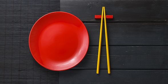 Empty ceramic dish or plate and asian chopsticks on black wooden background