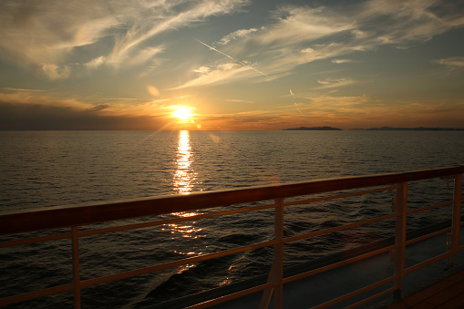 From the deck of a cruise ship at sunset looking over the ocean towards land in the distance.