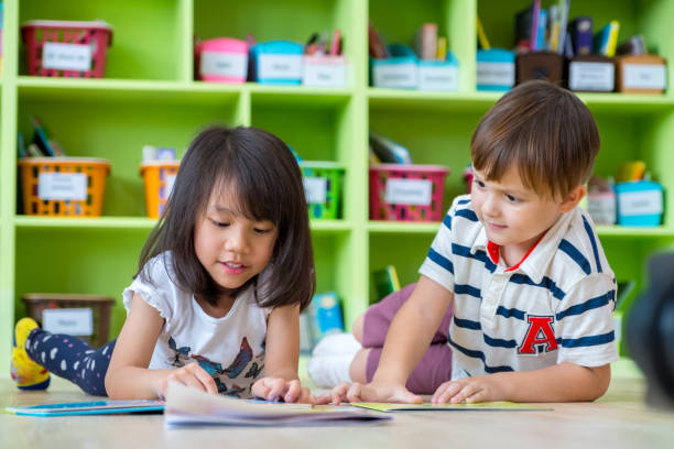 istock Two kid lay down on floor and reading tale book in preschool library,Kindergarten school education concept. 946804414