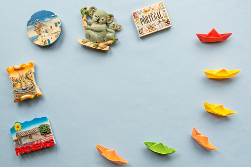 colorful paper ships and  various souvenir magnets from several world country arranged on the blue background