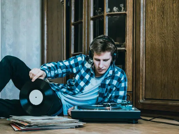 Photo of portrait of young man at home listening to the vinyl records, relaxing and dreaning
