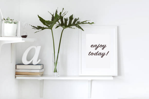 istock Stylish scandi interior with white shelf , mock up frame, books and hourglass. Design space of living room.. 946819954