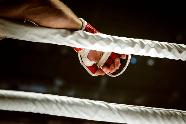 Red boxing gloves resting on a ring corner with blue canvas and white ropes, perfect for training, competition and fitness concepts with clean copy space.