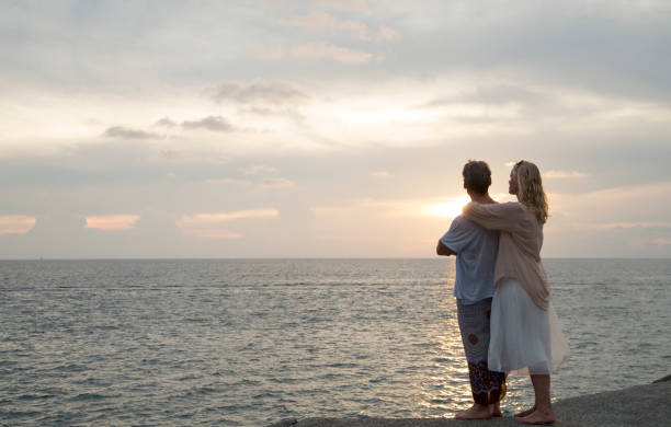 couple regarde dehors à la mer au coucher du soleil - women sarong beach white photos et images de collection