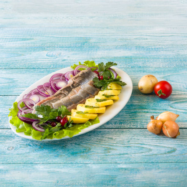 Homemade salted herring cut into pieces on a plate with green and salad onions, selective focus