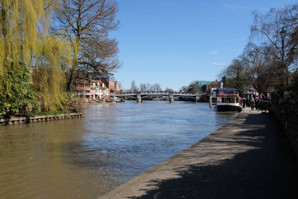 The River Thames and pedestrian bridge seen from Windsor, England, in early morning in spring Windsor and Eton, England - April 5, 2018: view of the River Thames and the Windsor Town Bridge - or Eton Bridge - connecting Windsor (right) with Eton (left). Completed in 1824, this Georgian structure is now the oldest cast iron arch bridge crossing the Thames. It was fully pedestrianised in the 1970s due to cracks in the iron from heavy traffic.  It is a popular tourist destination, and the river is used by numerous pleasure boats. The photo is taken from an embankment in Windsor, with a small island to the left containing trees and shrubs. thames river photos stock pictures, royalty-free photos & images