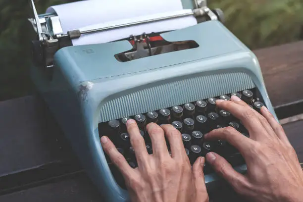 male hands writing with an old blue typewriter, vintage stock photo