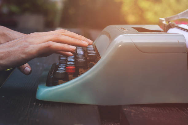 Blurred hands typing on a retro white typewriter in a dark moody setting. Yellow paper with typed text graces the machine, evoking creativity and timeless nostalgia.