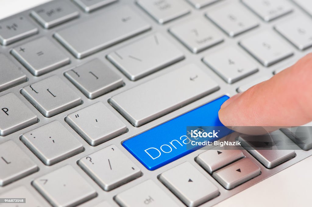 A finger press blue Donate button on laptop keyboard A finger press blue Donate button on laptop keyboard. Charitable Donation Stock Photo