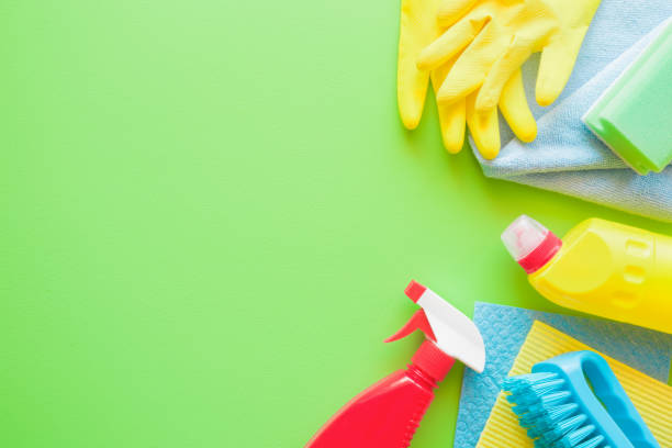 istock Colorful cleaning set for different surfaces in kitchen, bathroom and other rooms. Empty place for text or logo on green background. Cleaning service concept. Spring regular clean up. Top view. 946877244