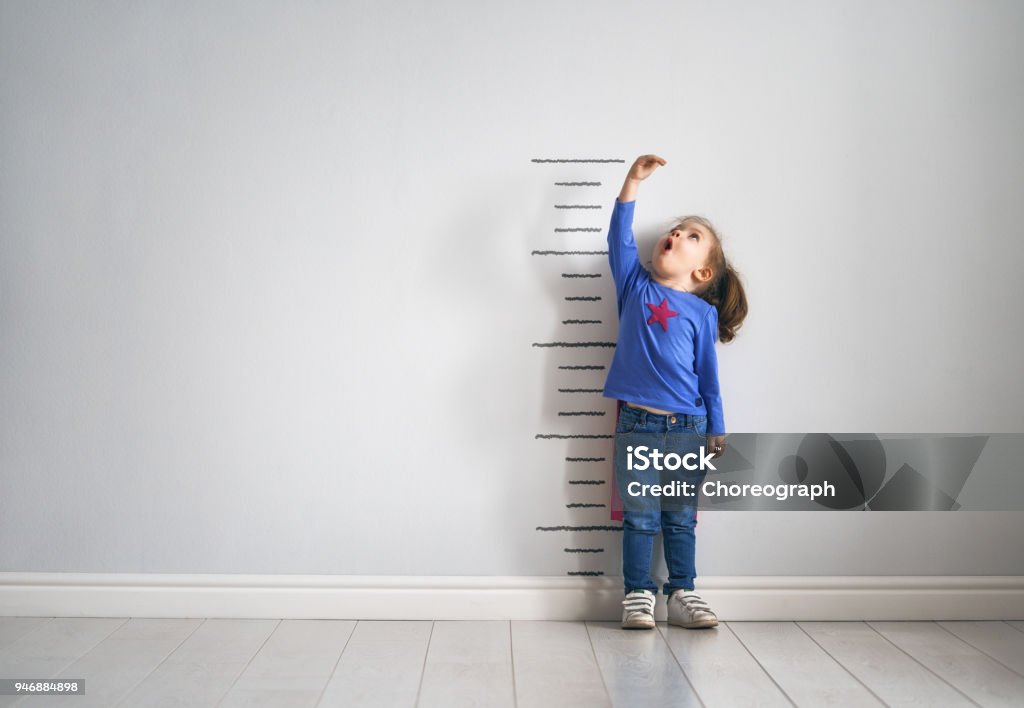 child is playing superhero Little child is playing superhero. Kid is measuring the growth on the background of wall. Girl power concept. Child Stock Photo