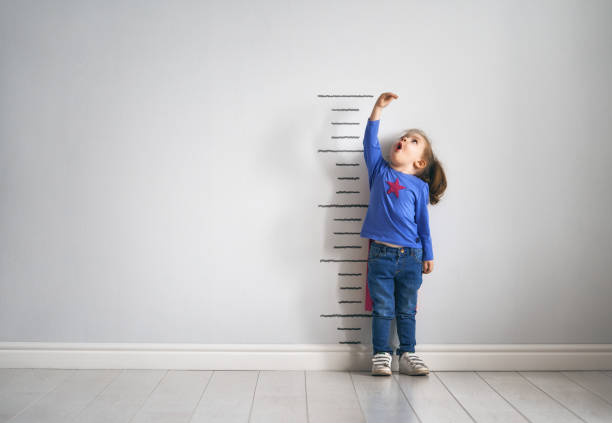 child is playing superhero Little child is playing superhero. Kid is measuring the growth on the background of wall. Girl power concept. measuring stock pictures, royalty-free photos & images