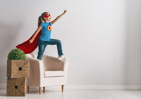 Little child is playing superhero. Kid on the background of bright wall. Girl power concept.