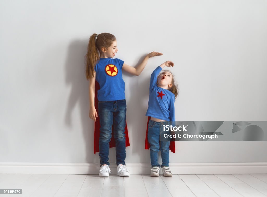 children are playing superhero Two little children are playing superhero. Kids are measuring the growth on the background of wall. Girl power concept. Short - Length Stock Photo