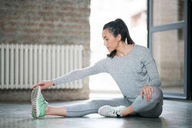 Stretching Hamstrings Beautiful young woman sitting on the floor and stretching her muscles after daily workout. Progressive Muscle Relaxation stock pictures, royalty-free photos & images