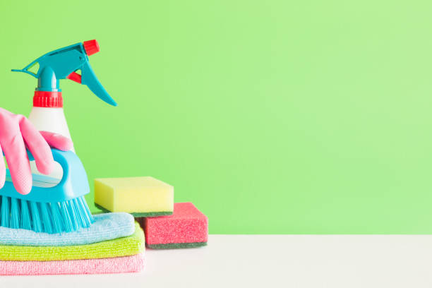 istock Colorful cleaning set for different surfaces in kitchen, bathroom and other rooms. Empty place for text or logo on green background. Cleaning service concept. Spring regular clean up. Front view. 946909734