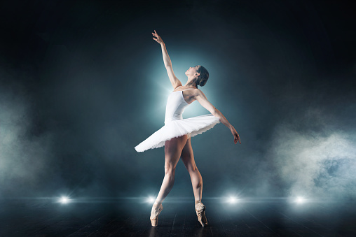 Graceful Ballet Beauty. Athlete showcases ballet prowess in white tutu against white studio backdrop, her shadow repeats her fluid movements. Concept of grace, art and beauty, ballet, athleticism.